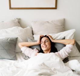 Zadowolona, wyspana kobieta leży w swoim łóżku.