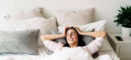 Zadowolona, wyspana kobieta leży w swoim łóżku.