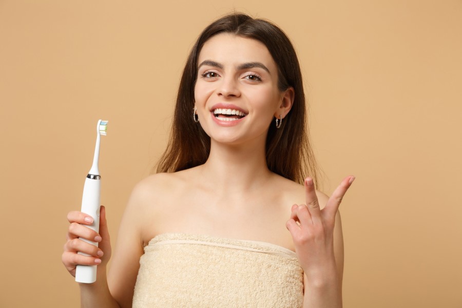 Uśmiechnięta kobieta korzysta ze szczoteczki sonicznej.
