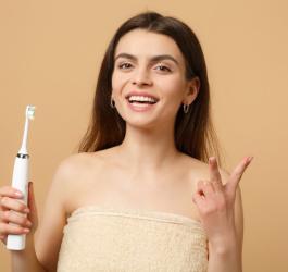 Uśmiechnięta kobieta korzysta ze szczoteczki sonicznej.
