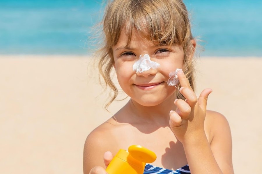 Dziewczynka nakłada na skórę twarzy krem z filtrem.