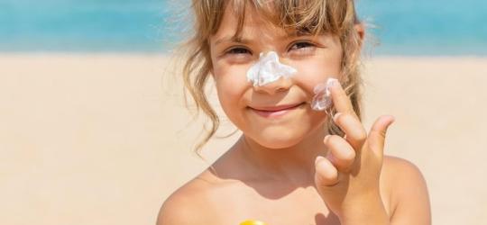 Dziewczynka nakłada na skórę twarzy krem z filtrem.