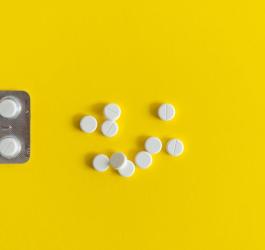 Blister oraz białe tabletki leżące na żółtym tle.