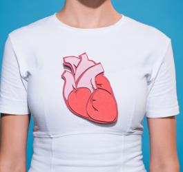 Kobieta w białym t-shircie. Na koszulkę naniesiono papierowy model ludzkiego serca.