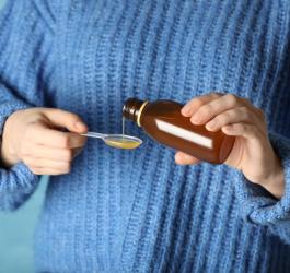 Kobieta nalewa na łyżeczkę porcję syropu na kaszel.