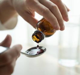 Osoba odmierza porcję syropu na łyżeczkę.