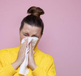 Kobieta cierpiąca na alergię krzyżową wydmuchuje nos w chusteczkę.
