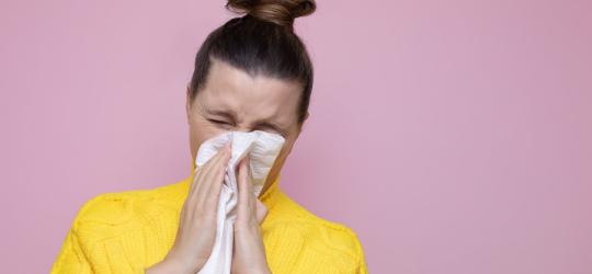 Kobieta cierpiąca na alergię krzyżową wydmuchuje nos w chusteczkę.