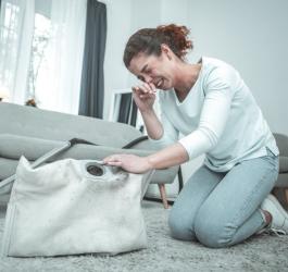Kobieta czyści worek z odkurzacza, zmaga się z objawami alergii na kurz.