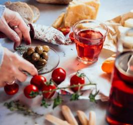 Kobieta sięga po jedzenie, obok stoi szklanka oraz butelka z alkoholem.