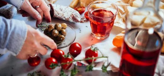 Kobieta sięga po jedzenie, obok stoi szklanka oraz butelka z alkoholem.