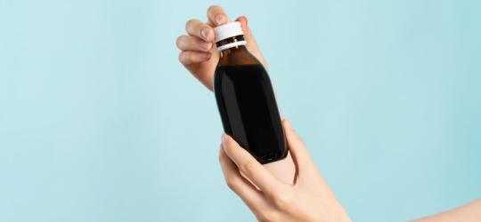 Kobieta trzyma w dłoniach buteleczkę syropu z ambroksolem.