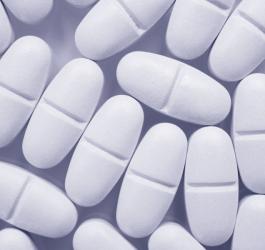 Białe, owalne tabletki z podziałką, rozsypane na jasnym tle.