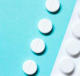 Białe tabletki i blister leków na turkusowym tle.