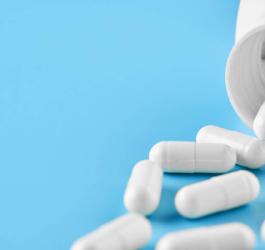 Biały kapsułki wysypujące się z białej buteleczki.