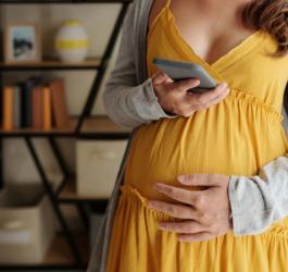 Ciężarna kobieta sprawdza na telefonie wyniki badań prenatalnych.