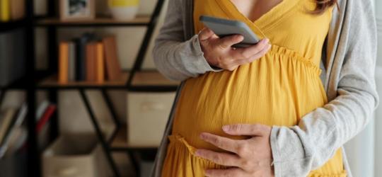 Ciężarna kobieta sprawdza na telefonie wyniki badań prenatalnych.