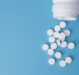 Błękitne tło. Białe tabletki wysypują się z plastikowej, białej buteleczki.