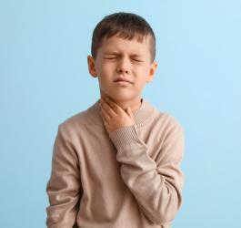 Chłopiec trzyma się za szyję, boli go gardło, co jest jednym z licznych objawów błonicy.