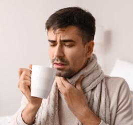 Przeziębionego mężczyznę boli gardło przy przełykaniu ulubionej herbaty.