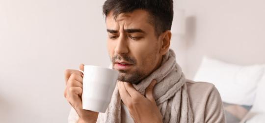 Przeziębionego mężczyznę boli gardło przy przełykaniu ulubionej herbaty.