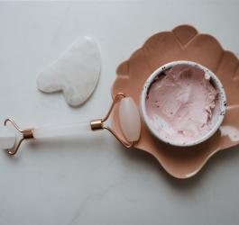 Roller i kamień gua sha do masażu twarzy oraz miseczka wypełniona kremem lub maseczką do twarzy.