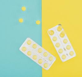 Blister z żółtymi tabletkami na niebiesko-żółtym tle. 3 tabletki znajdują się poza blistrem.
