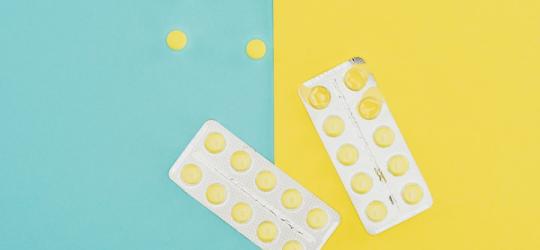 Blister z żółtymi tabletkami na niebiesko-żółtym tle. 3 tabletki znajdują się poza blistrem.