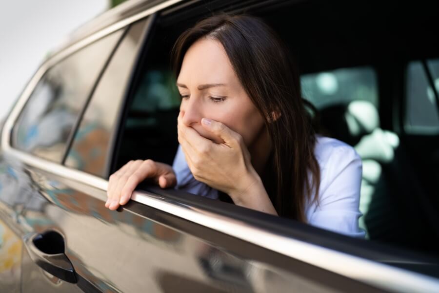 Kobieta siedzi w samochodzie przy otwartym oknie, dokuczają jej objawy choroby lokomocyjnej.