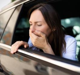 Kobieta siedzi w samochodzie przy otwartym oknie, dokuczają jej objawy choroby lokomocyjnej.