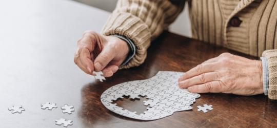 Mężczyzna chorujący na chorobę Parkinsona układa puzzle o kształcie głowy widzianej z profilu.