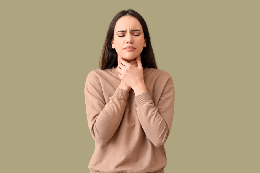 Kobiecie dokucza chrypka, trzyma się za szyję.