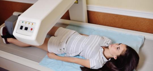 Kobieta podczas densytometrii - leży na stole urządzenia.