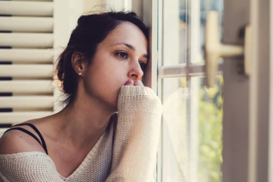 Smutna kobieta wygląda przez okno.