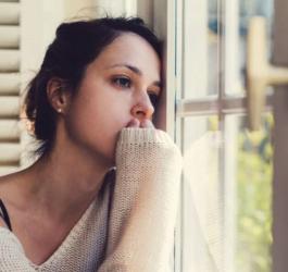 Smutna kobieta wygląda przez okno.