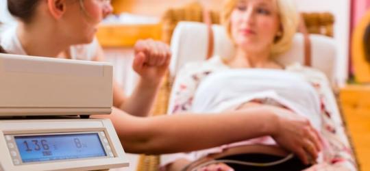 Położna przeprowadza u kobiety w ciąży badanie przy pomocy detektora tętna płodu.