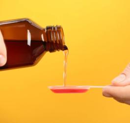 Osoba nalewa na łyżeczkę porcję syropu na kaszel.
