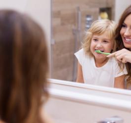 Mama uczy swoją córkę poprawnego szczotkowania zębów.