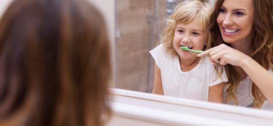 Mama uczy swoją córkę poprawnego szczotkowania zębów.