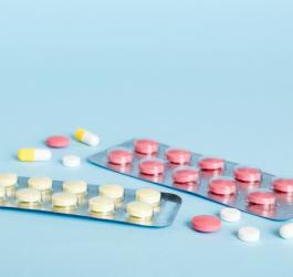 Blistry z żółtymi oraz różowymi tabletkami, a także rozsypane obok kolorowe tabletki i kapsułku.