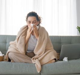 Kobieta choruje na grypę, siedzi na kanapie i wydmuchuje nos.