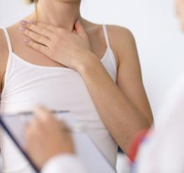 Kobieta w gabinecie endokrynologicznym, choruje na Hashimoto, trzyma się za szyję.