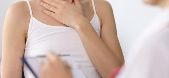 Kobieta w gabinecie endokrynologicznym, choruje na Hashimoto, trzyma się za szyję.