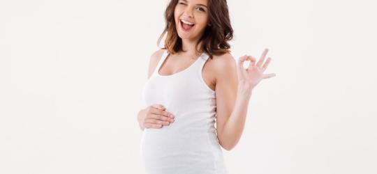 Radosna, uśmiechnięta kobieta w zaawansowanej ciąży.