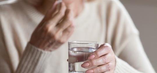 Dojrzała kobieta zażywa tabletkę będącą hormonalną terapią zastępczą.