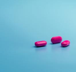 Różowe tabletki na turkusowym tle, zawierające ibuprofen.