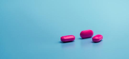 Różowe tabletki na turkusowym tle, zawierające ibuprofen.