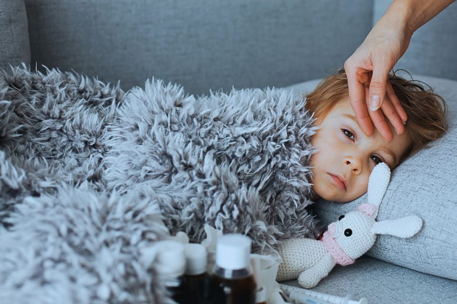 Przeziębione dziecko leży na kanapie, mama sprawdza temperaturę jego czoła.