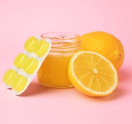 Pastylki na gardło w blistrze oparte o słoik miodu i cytrynę.