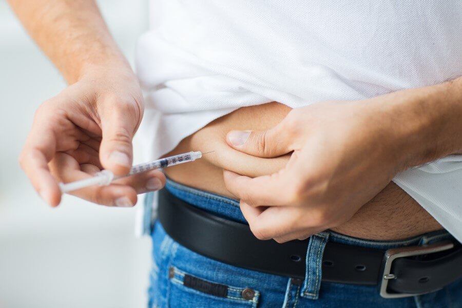 Mężczyzna chory na cukrzycę wstrzykuje sobie insulinę w okolicy brzucha.